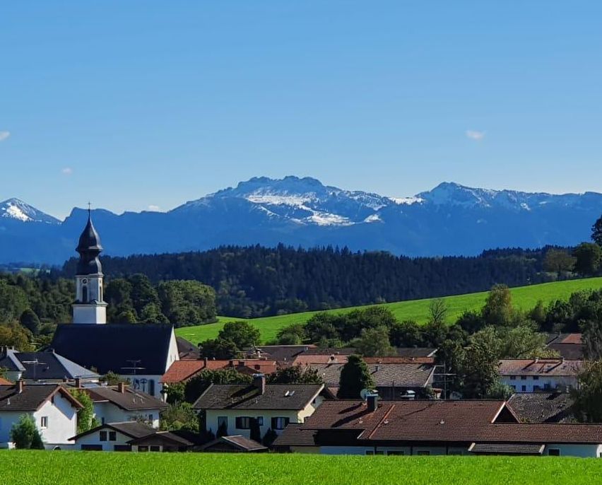 Ein malerisches Dorf in einem grünen Tal mit einer Kirche und Bergen im Hintergrund.