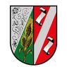 Ein Schild, das durch einen diagonalen Streifen in einen grünen und roten Bereich geteilt ist. Es zeigt links eine Weizengarbe und rechts zwei Schriftrollen.