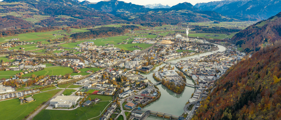 Luftaufnahme einer Stadt mit Fluss, Bergen, Gebäuden und grünen Feldern.