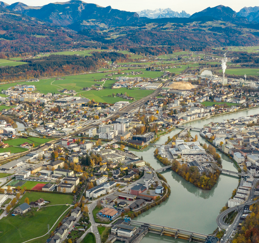 Luftaufnahme einer Stadt mit Fluss, Bergen, Gebäuden und grünen Feldern.