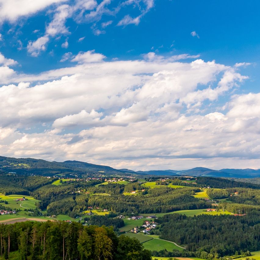 Luftaufnahme eines üppig grünen Tals mit Häusern und Bergen unter einem blauen Himmel mit verstreuten Wolken.