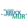 Das Logo der Stadt Bruck an der Mur zeigt die Wörter 'Die Stadt Bruck an der Mur' in blauen und grünen Schriften. Das Wort 'Die' steht links, und 'Stadt' ist über 'Bruck'. 'An der Mur' ist in einer kleineren Schrift unter dem Haupttext geschrieben.