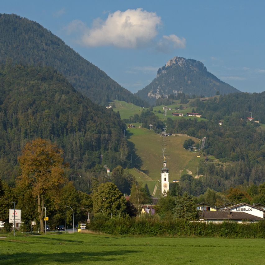 Ein Panoramablick auf Berge und ein Dorf im Tal. Der Himmel ist klar mit einigen Wolken.