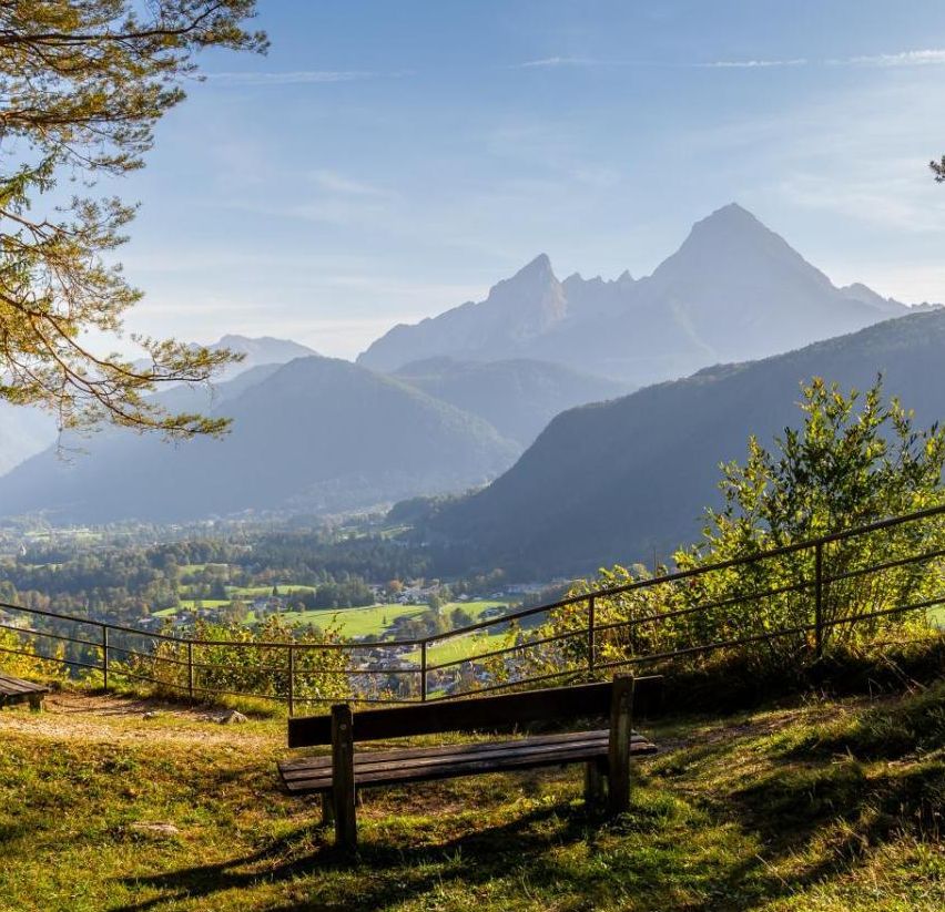 Ein friedlicher Bergblick mit zwei Bänken auf einem Grashügel, der einen Blick auf ein Tal und einen klaren blauen Himmel bietet.