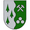 Ein Schild, das durch eine wellenförmige Linie geteilt ist. Links drei grüne Bäume. Rechts ein gekreuzter Hammer und drei weiße Baumstämme.