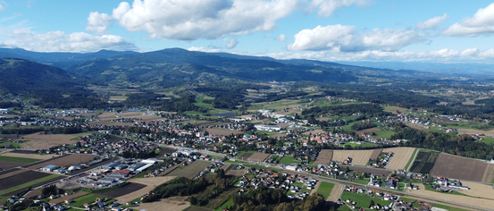 Luftaufnahme einer Stadt umgeben von Feldern, Bergen und einem klaren blauen Himmel mit verstreuten Wolken.
