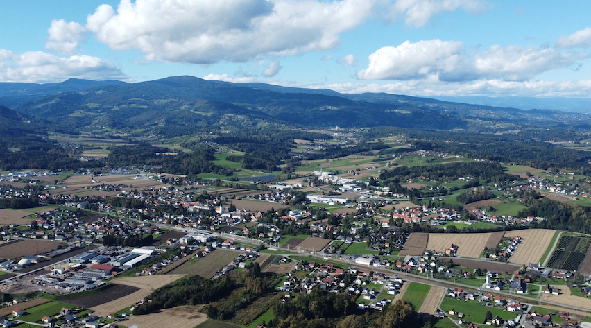 Luftaufnahme einer Stadt umgeben von Feldern, Bergen und einem klaren blauen Himmel mit verstreuten Wolken.