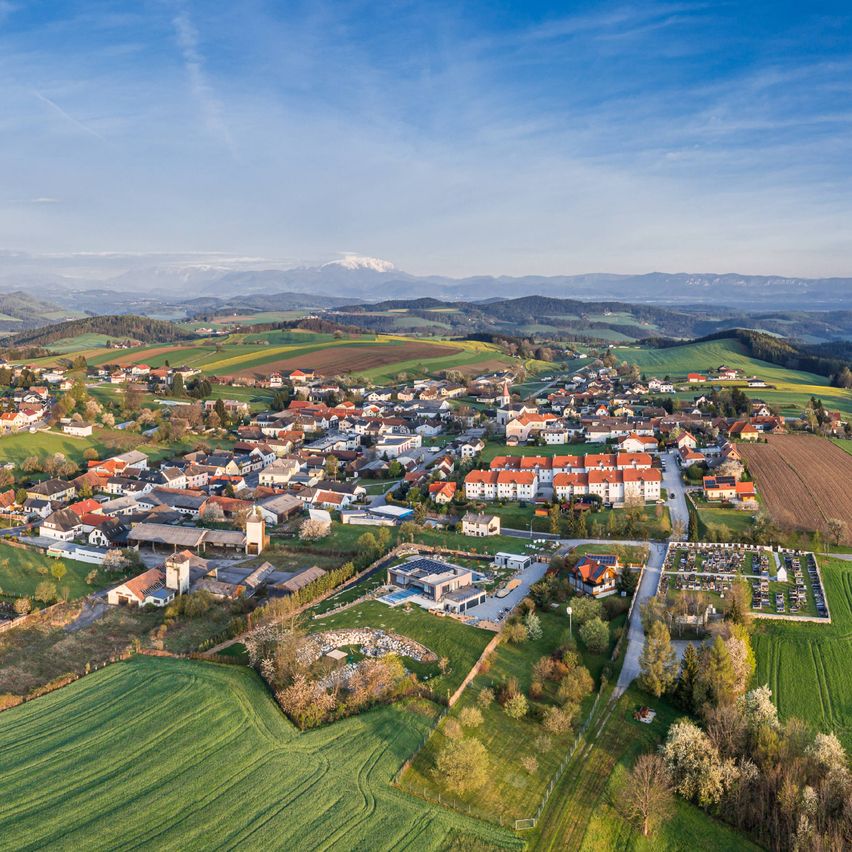 Eine Luftaufnahme einer Stadt mit vielen Gebäuden und Häusern, grünen Feldern und Bergen in der Ferne.