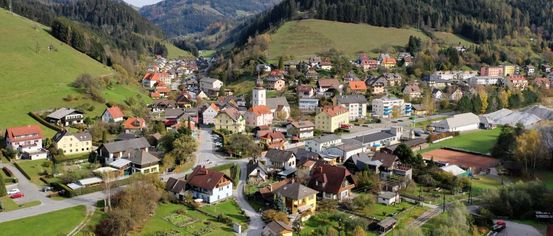 Luftaufnahme eines kleinen Dorfes in den Bergen, mit Häusern in verschiedenen Farben und einer Kirche in der Mitte.