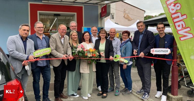 Eine Gruppe von Menschen, darunter Männer und Frauen, versammelt sich vor einem Geschäft und schneidet ein Band mit Scheren. Sie lächeln und posieren für ein Foto.