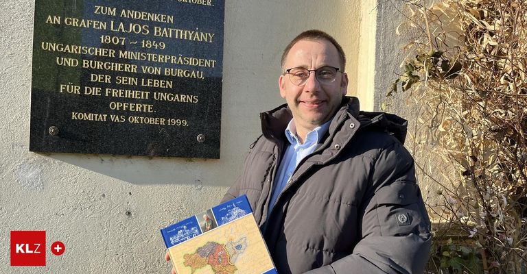 Ein Mann hält ein Buch vor einer Gedenktafel, die Lajos Batthyány, den ersten Ministerpräsidenten Ungarns, ehrt.