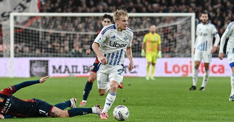 Ein Fußballspieler in einem weißen Trikot mit Uber auf dem Jersey läuft auf das Tor zu, ein anderer Spieler liegt hinter ihm auf dem Boden. Der Torwart steht in der Nähe des Tores. Das Spielfeld hat weiße Linien und Werbung an den Barrieren.