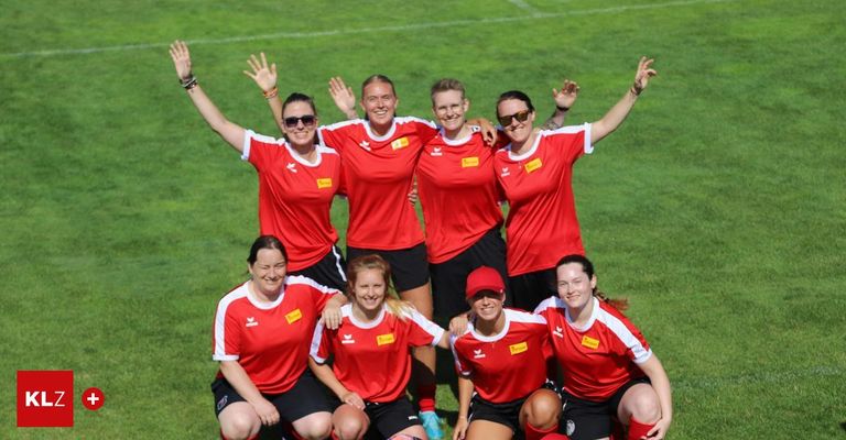 Eine Gruppe von weiblichen Fußballspielerinnen in roten Trikots und schwarzen Shorts posiert für ein Foto auf einem Rasenfeld mit erhobenen Armen.