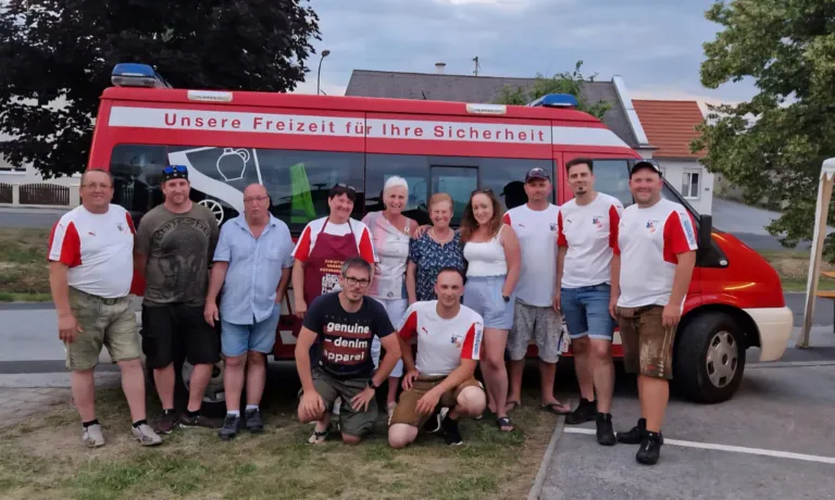 Eine Gruppe von Menschen in Freizeitkleidung steht vor einem roten Notfallfahrzeug. Sie lächeln für ein Foto, wobei ein Mann in einem Denim-Shirt in der Mitte kniet.