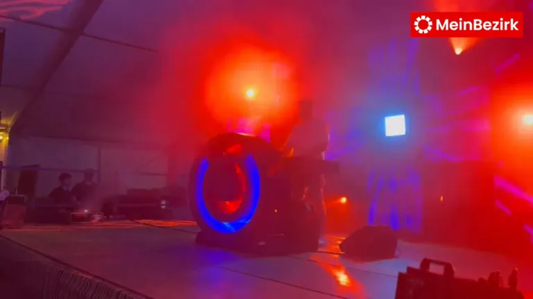 Eine Bühne mit rotem und blauem Lichtspiel, einer Person vor einem Lautsprecher und einem großen radähnlichen Objekt, das blaue und rote Licht ausstrahlt.