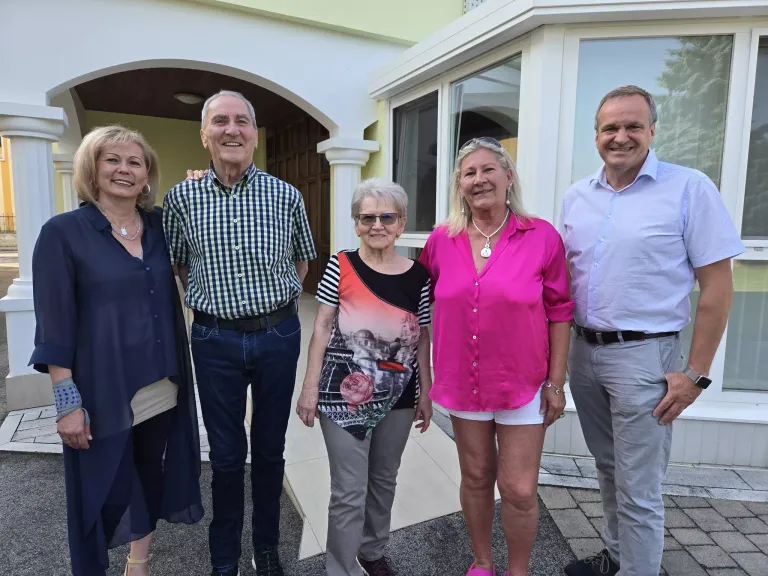 Fünf Erwachsene, vier Frauen und ein Mann, lächeln und posieren für ein Foto vor einem Gebäude.