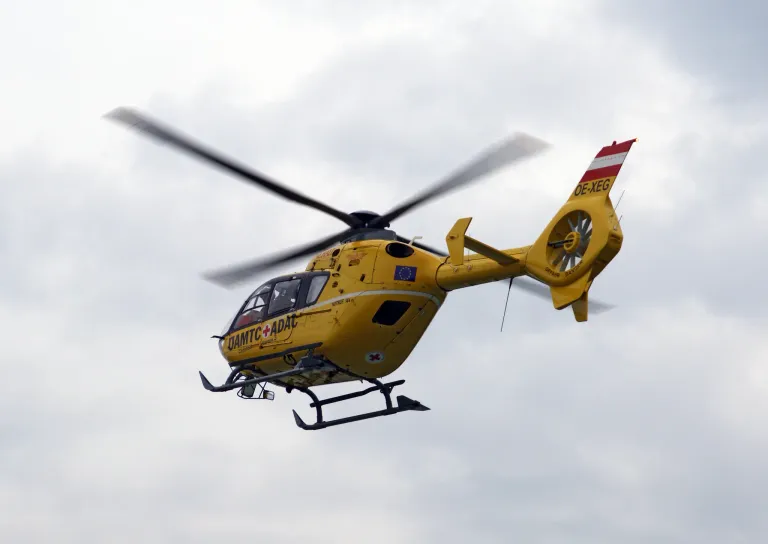 Ein gelber Hubschrauber mit rotem Kreuz und der Registrierungsnummer OE-XEG fliegt am Himmel.