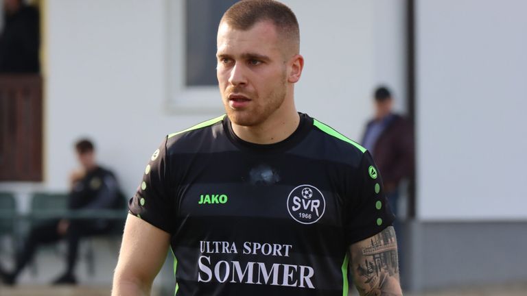 Ein Mann trägt ein schwarzes Shirt mit den Worten 'Ultra Sport Sommer' und einem Logo. Er hat ein Tattoo am rechten Arm.
