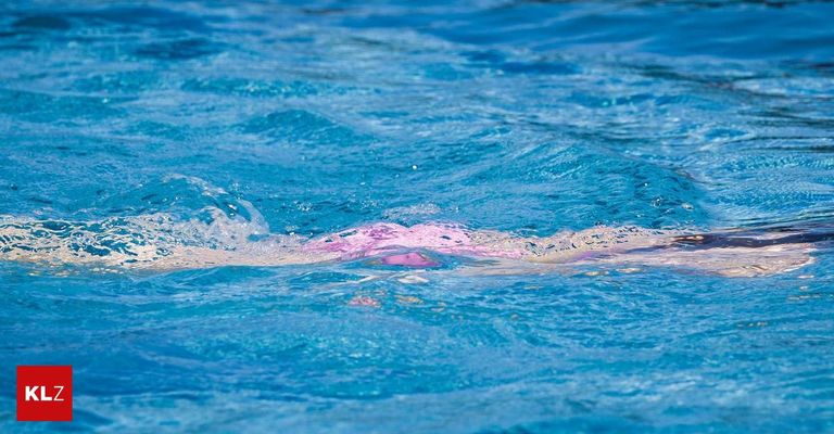 Eine Person schwimmt in einem blauen Pool und erzeugt mit ihren Bewegungen Wellen im Wasser. Das Wasser ist klar und reflektiert das Licht.