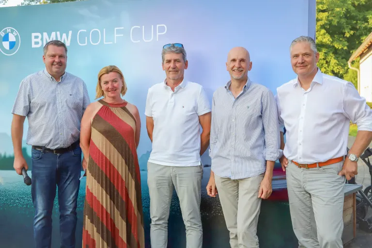 Fünf Personen stehen gemeinsam vor einem Banner mit der Aufschrift 'W Golf Cup'. Sie alle scheinen für die Kamera zu lächeln.