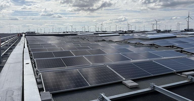 Solarmodule sind auf dem Dach eines Gebäudes installiert. Viele Windturbinen sind in der Ferne sichtbar.