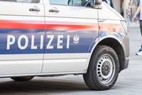 Ein Polizeiwagen ist am Straßenrand geparkt. Er hat blaue und weiße Streifen und das Wort 'POLIZEI' in Fettschrift. Das Rad des Wagens ist sichtbar und steht auf einer Betonfläche.