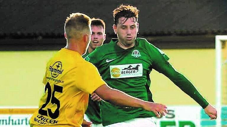 Drei Fußballspieler sind auf einem Feld. Der Spieler in Grün greift nach dem Ball. Der Spieler in Gelb blockt ihn. Der Spieler im Hintergrund beobachtet.