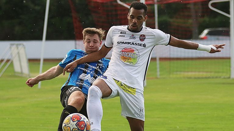 Zwei Fußballspieler sind auf dem Feld in Aktion. Einer in Weiß und der andere in Blau, sie kämpfen um den Ball.