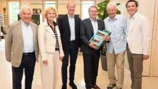 Sechs Menschen stehen in einer Gruppe. Ein Mann hält ein Buch und lächelt. Sie scheinen für ein Foto zu posieren.
