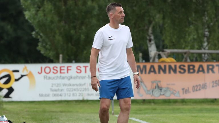 Ein Mann läuft auf einem Fußballfeld in einem weißen Nike-Shirt und blauen Shorts und sieht zur Seite.