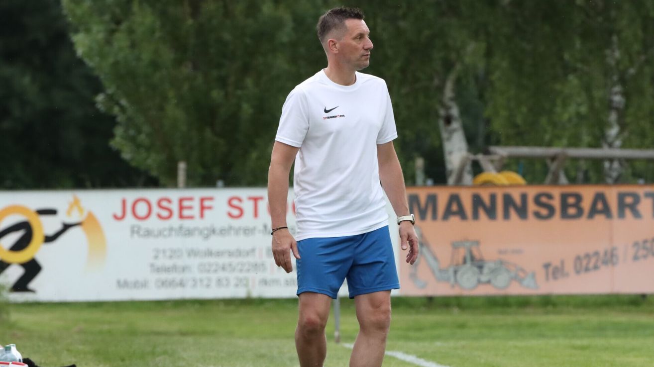 Ein Mann läuft auf einem Fußballfeld in einem weißen Nike-Shirt und blauen Shorts und sieht zur Seite.