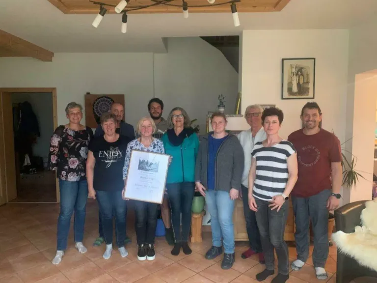 Eine Gruppe von Erwachsenen posiert für ein Foto in einem Raum mit einem Zertifikat, lächelt und trägt verschiedene Kleidungsstücke.