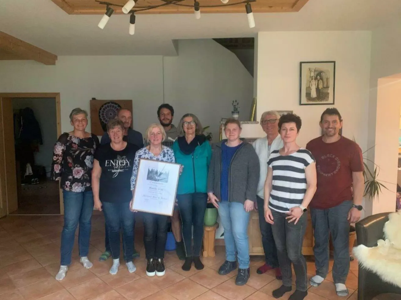 Eine Gruppe von Erwachsenen posiert für ein Foto in einem Raum mit einem Zertifikat, lächelt und trägt verschiedene Kleidungsstücke.