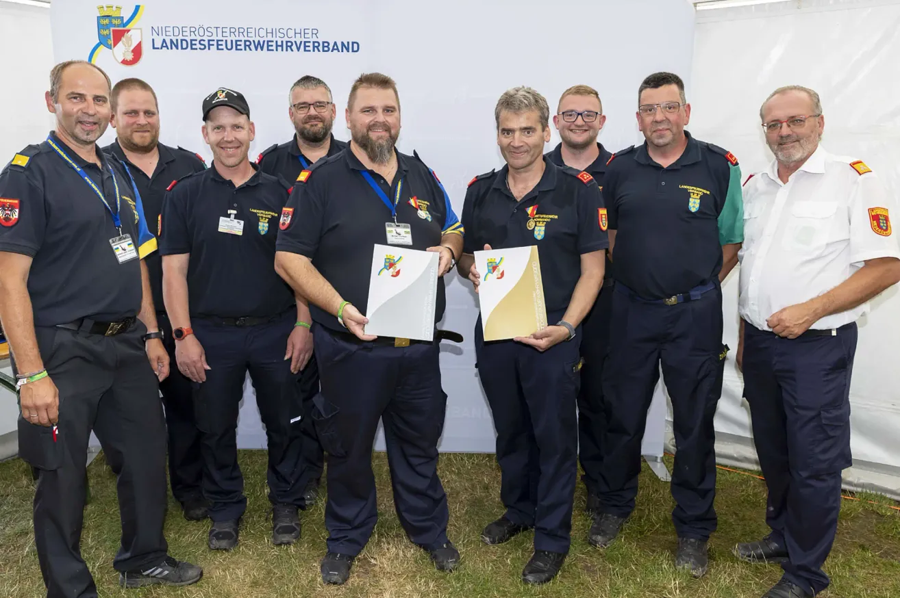Eine Gruppe von Feuerwehrleuten des Niederösterreichischen Landesfeuerwehrverbandes steht zusammen und hält Auszeichnungen. Sie tragen alle Uniformen und stehen auf Gras.