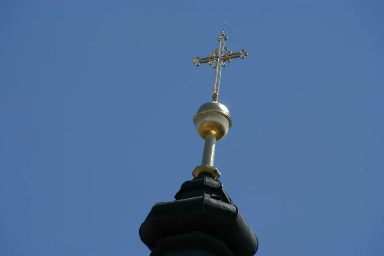Ein goldenes Kreuz auf der Spitze einer turmförmigen Struktur unter einem klaren blauen Himmel.