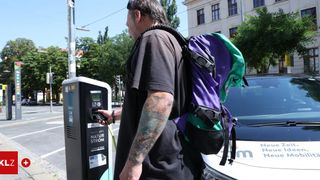 Ein Mann mit Tätowierungen und einem Rucksack lädt ein Elektroauto an einer Ladestation auf.