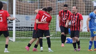 Eine Gruppe von Fußballspielern feiert vor einem Tor. Ein Spieler trägt ein rotes Trikot mit der Nummer 14. Ein anderer trägt die Nummer 87.