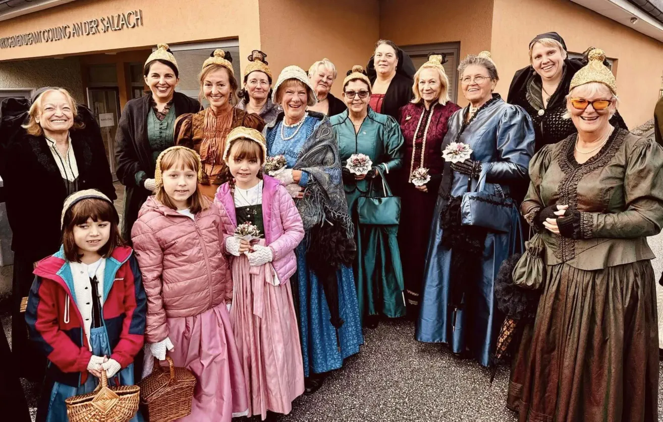 Eine Gruppe von Frauen und Mädchen in Vintage-Kleidung, die vor einem Gebäude für ein Foto posieren.