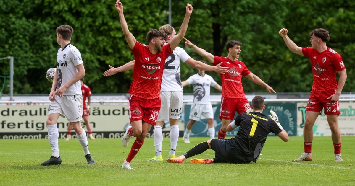Fußballspieler in Rot feiern ein Tor, ein Spieler in Weiß fällt auf den Boden, umgeben von Spielern in weißen und roten Trikots.