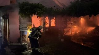 Ein Feuerwehrmann löscht ein Feuer in einem Gebäude, mit Schildern, die 'Hoiturfahrt' und 'Stada Privata' auf den Wänden anzeigen.