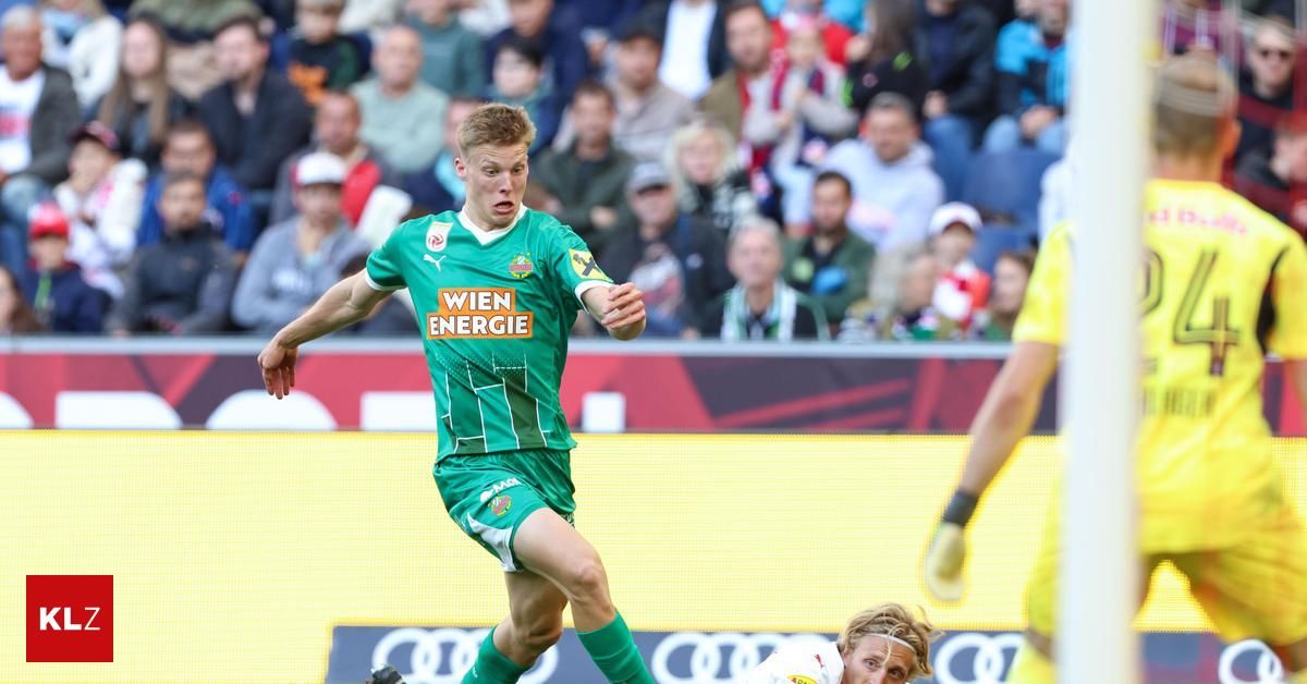 Ein Fußballspieler in einem grünen Trikot mit 'Wien Energie' darauf läuft Richtung Tor, während ein anderer Spieler in Weiß versucht, ihn zu blockieren.