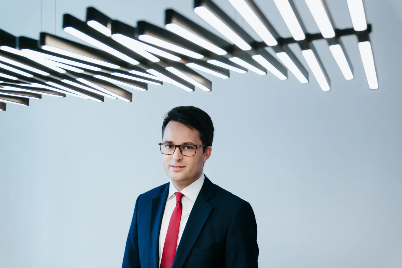 Ein Mann in Anzug und Krawatte steht unter einer Deckenbeleuchtung.