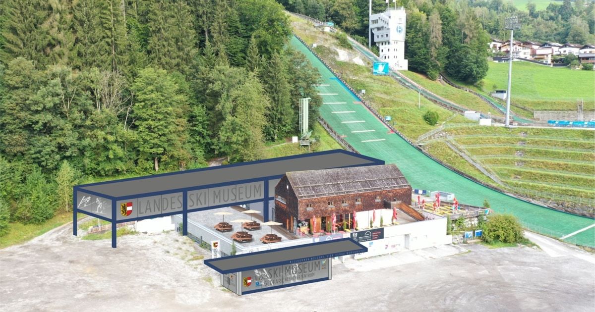 Ein Luftbild eines Skimuseums, umgeben von einem üppigen grünen Hang. Das Gebäude hat ein geneigtes Dach und ist mit 'Landes Ski Museum' beschriftet. Draußen sind Schirme aufgestellt.
