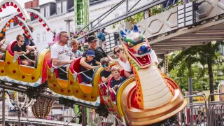 Eine Familie mit fünf Personen, darunter zwei Erwachsene und drei Kinder, genießt eine Fahrt auf einer farbenfrohen Drachen-Achterbahn in einem Vergnügungspark.