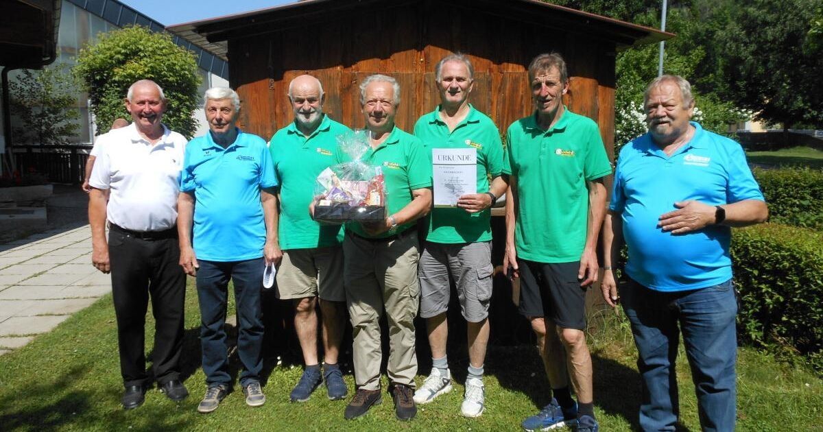 Eine Gruppe von Männern steht draußen, drei in grünen Shirts und einer hält ein Zertifikat. Sie lächeln und scheinen für ein Foto zu posieren.