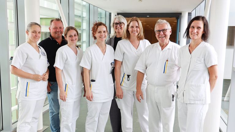 Eine Gruppe medizinischer Fachkräfte in weißen Uniformen lächelt und posiert für ein Foto in einem Krankenhausflur.