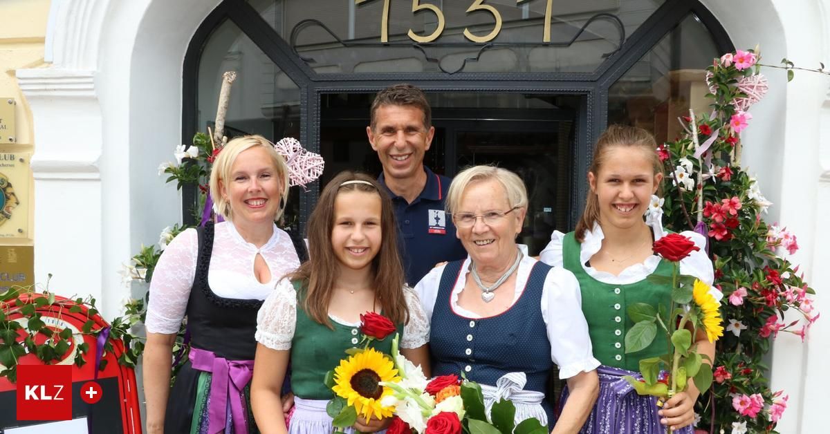 Fünf Personen stehen lächelnd vor einem Gebäudeeingang. Ein Mann in einem blauen Poloshirt steht in der Mitte. Drei Frauen und ein Mädchen in traditioneller bayerischer Kleidung halten Blumen. Das Gebäude hat ein Schild mit der Nummer 1531.