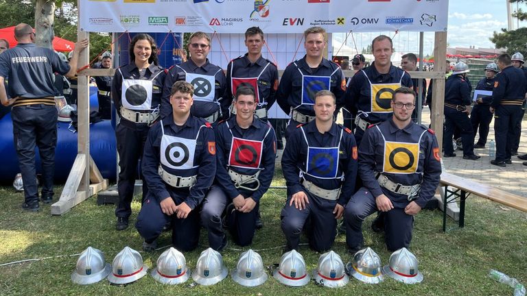 Eine Gruppe von Feuerwehrleuten in Uniformen posiert für ein Foto mit Helmen vor einem Banner.