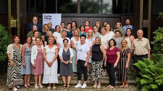 Eine Gruppe von Menschen, darunter Frauen und Männer, stehen zusammen für ein Foto, einige tragen Brillen, Halsketten und Armbänder. Sie stehen auf Stufen und scheinen für ein Gruppenfoto vor einem Gebäude zu posieren.