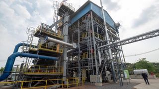 Eine große Industrieanlage mit Metallstrukturen und Rohrleitungen, gelben Geländern und einem klaren blauen Himmel im Hintergrund.